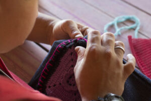 Foto em close de duas mãos costurando uma peça de tecido