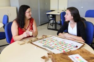 Foto de duas mulheres ao redor de uma mesa. Sobre a mesa há um cronograma.