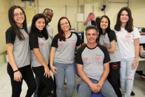 Foto de cinco mulheres e dois homens posando para uma fotografia. Um dos homens está no centro da imagem com mulheres ao lado.