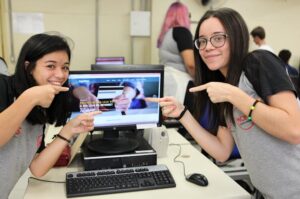 Foto de duas jovens apontando para a tela de um computador e sorrindo