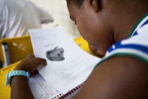 Foto da lateral do rosto de uma criança lendo um papel durante a aula.