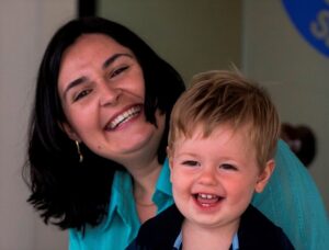 Foto de uma mulher com uma criança no colo. Os dois sorriem.