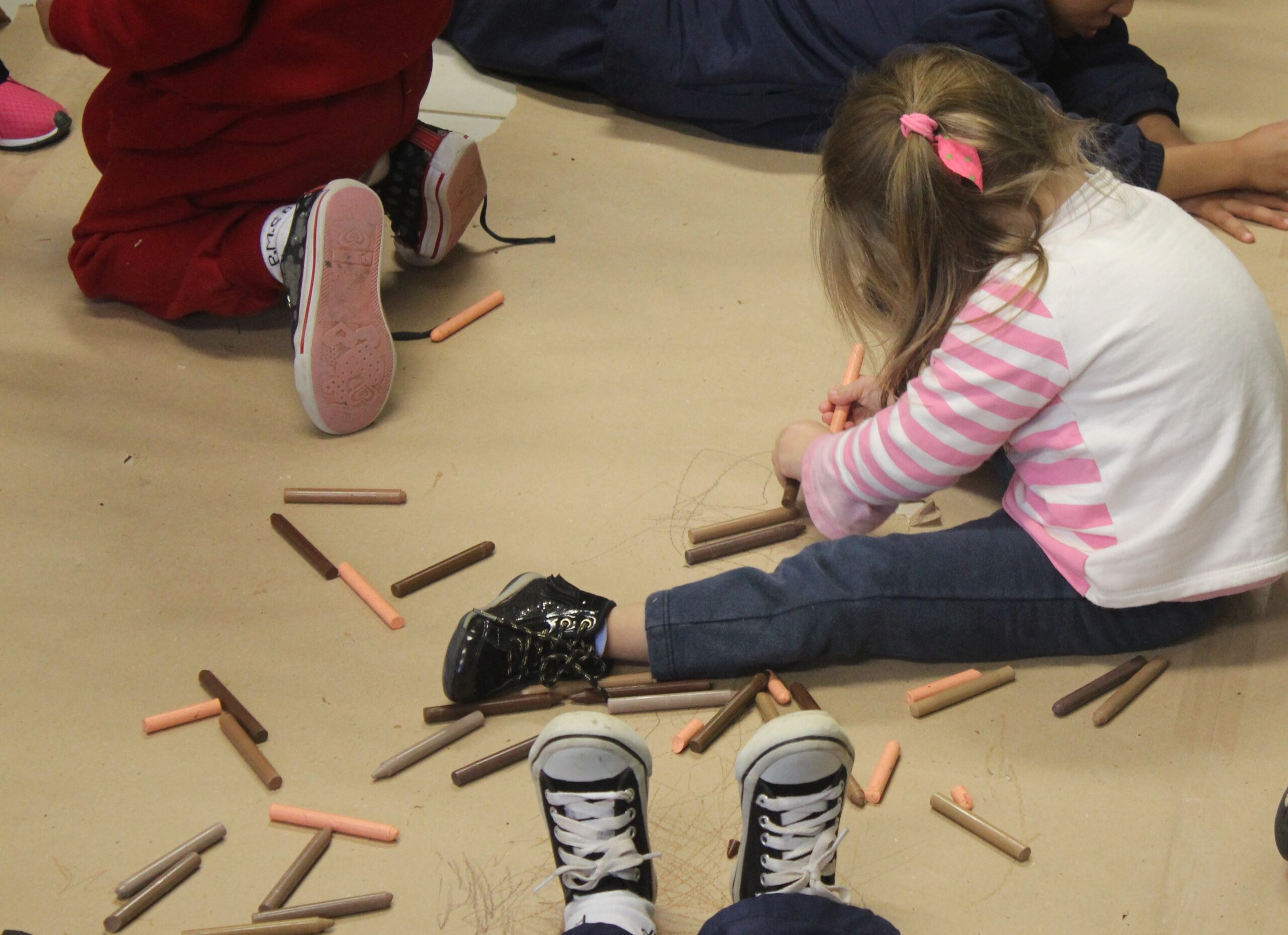 Aluna de educação infantil brinca com giz e desenha sentada ao chão.