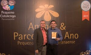 Funcionário da Volkswagen segura troféu da homenagem recebido do diretor do Pequeno Cotolengo, em nome da Fundação Volkswagen