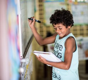 Aluno sorri enquanto passa para lousa o conteúdo do caderno.