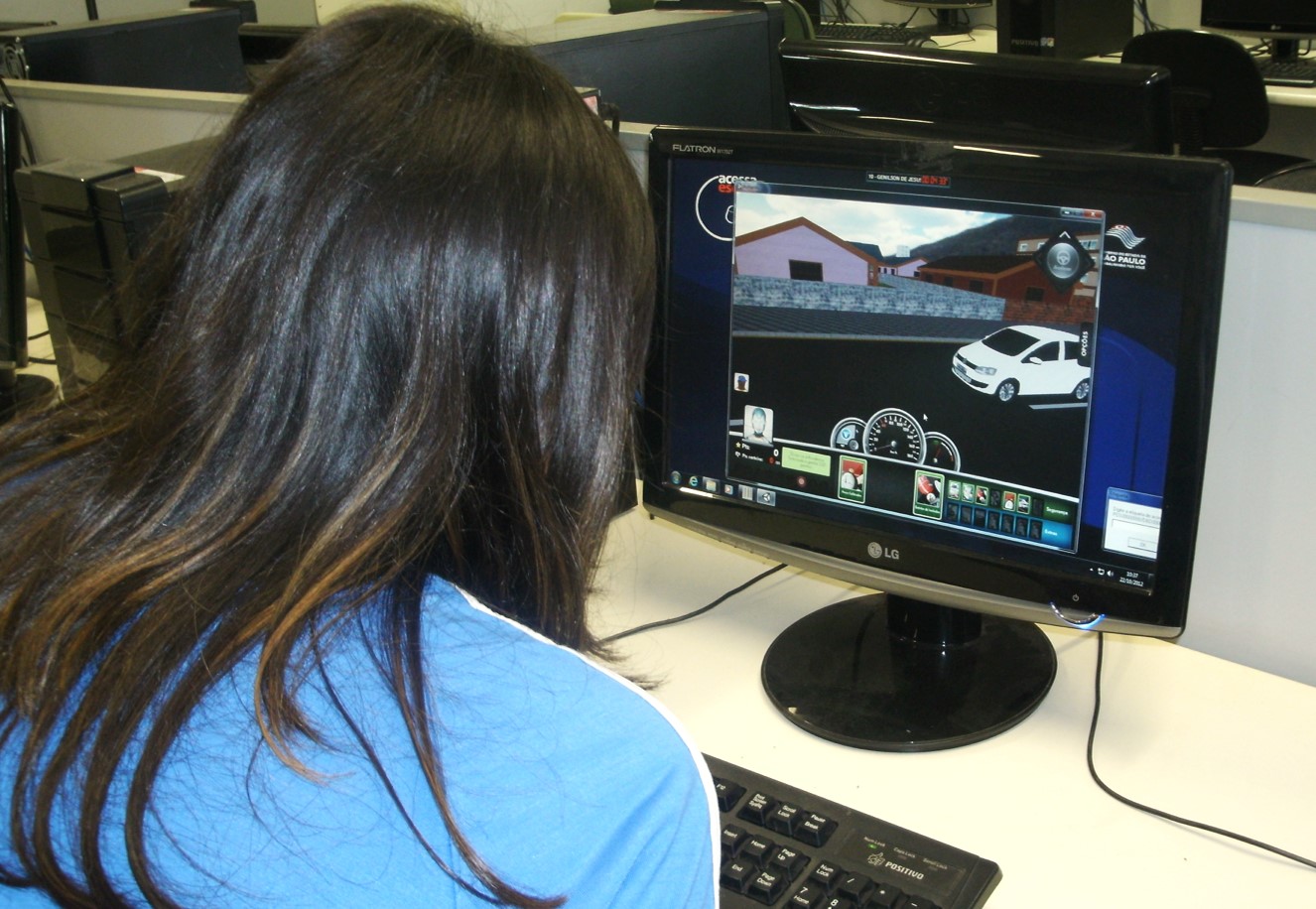 Aluna de costas olha para um monitor de computador com atividade do projeto Jogo da Vida em Trânsito na tela.