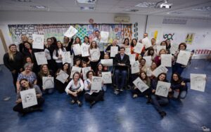 Foto de participantes da oficina de artes. Eles seguram seu desenhos em torno de Rodrigo Mendes.