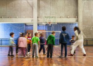 Foto de alunos interagindo entre si e com professores no centro de uma quadra de esportes..