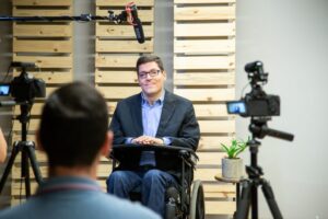 Foto dos bastidores da entrevista com Rodrigo Mendes está em sua cadeira de rodas, cercado por câmeras e microfones