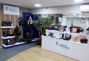 Expositores com produtos feitos pelas empreendedoras participantes do projeto Costurando o Futuro. Ao fundo, destaque para banco de carro cercado por mochilas feitas por tecidos automotivos.