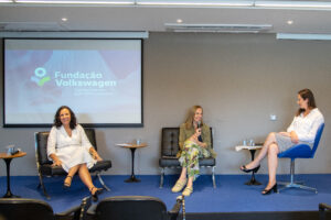 No palco do evento, especialistas dialogam sentadas em cadeiras.