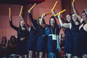 No palco, formandas do Costurando o futuro comemoram com seus canudos de certificado nas mãos.