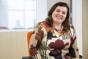 Mulher brança de cabelos castanhos sorri para a câmera