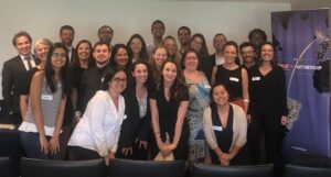 Grupo de homens e mulheres em pé, sorrindo, reunido para a foto; à direita, banner com informações do programa Skills for Prosperity