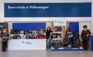 3 mulheres empreendedoras participantes do Costurando o Futuro sorriem em meio aos produtos do Bazar, dispostos em expositores