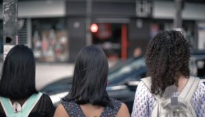 Cena do filme em que três meninas observam o trânsito de uma cidade enquanto esperam para atravessar uma rua.