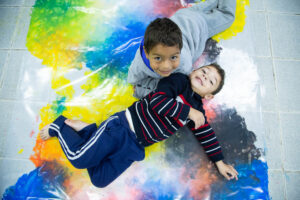 Foto de dois meninos deitados no chão. Eles estão olhando para cima e sorriem.