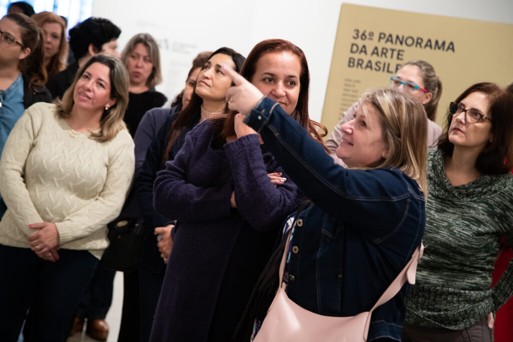 Foto de um grupo de mulheres em uma galeria. Ao centro, uma delas aponta para o lado esquerdo
