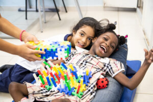 Aluna com e sem deficiência brincam com blocos de montar e sorriem para a câmera