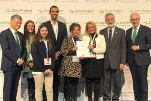Foto de um grupo de mulheres e homens em pé, lado a lado, sorrindo para a foto. Duas mulheres mostram uma folha.