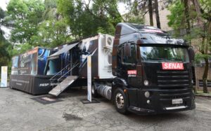 Foto de um caminhão de ensino móvel do SENAI estacionado em uma rua arborizada.