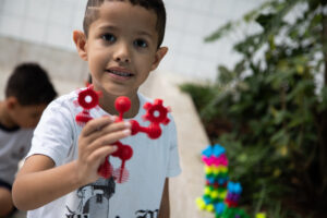 Foto de um menino sorrindo enquanto segura um brinquedo vermelho em uma das mãos
