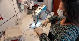 Foto de uma mulher usando uma máscara no rosto enquanto usa uma máquina de costura