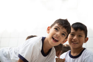 Foto de dois meninos sorrindo. Atrás deles aparecem outras crianças de costas.