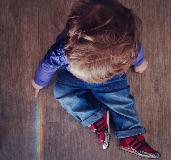 Foto de uma criança pequena, vista de cima, sentada em um piso de madeira.