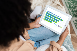 Foto de uma mulher sentada com um tablet apoiado em cima das pernas.